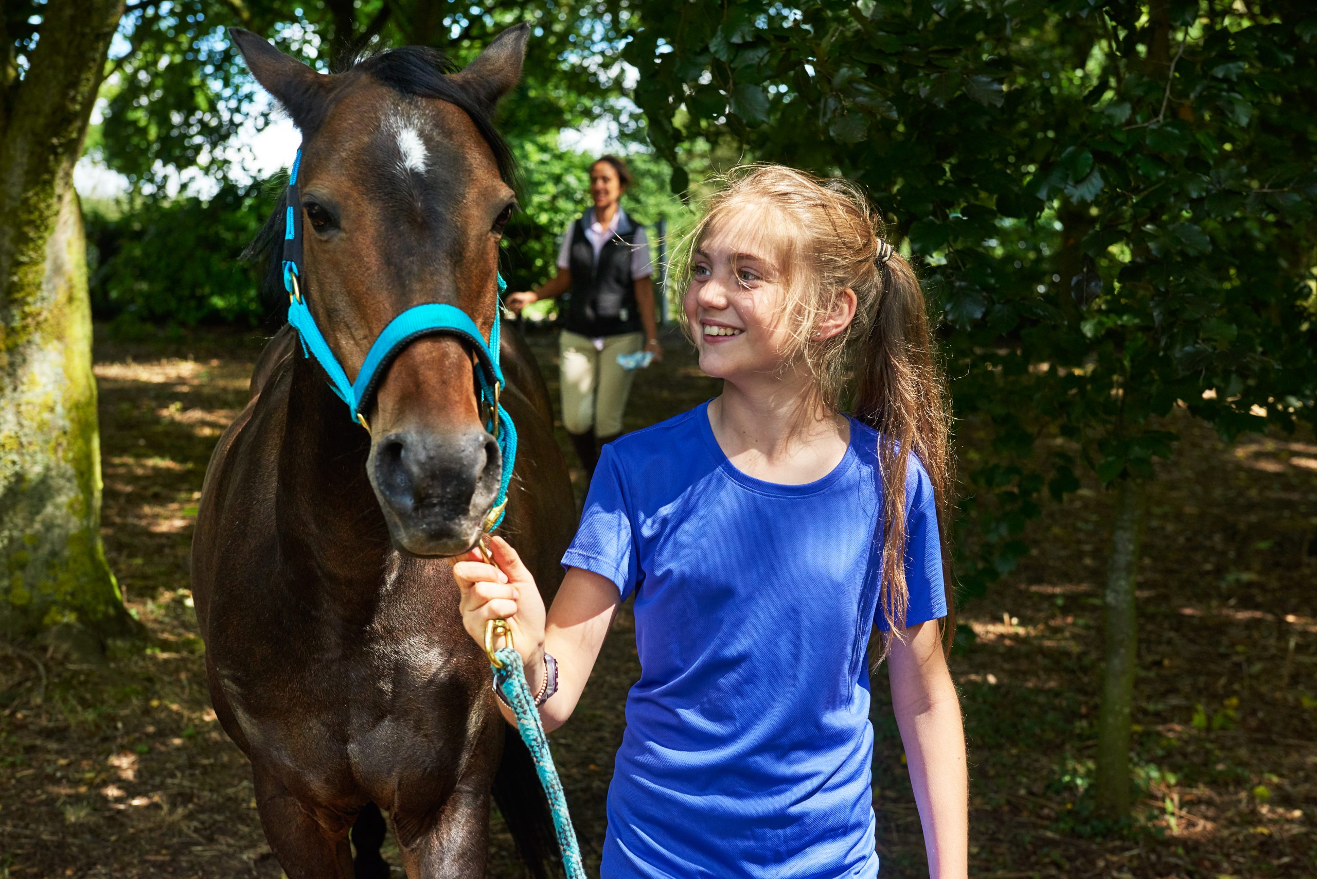 Girl holding lead rope looking at horse smiling Summer horseback camp kid walking a horse